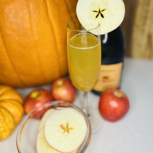 apple cider spritz in a champagne glass on a counter with apple and apple slices