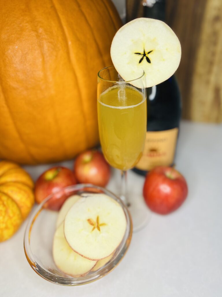 apple cider spritz in a champagne glass on a counter with apple and apple slices