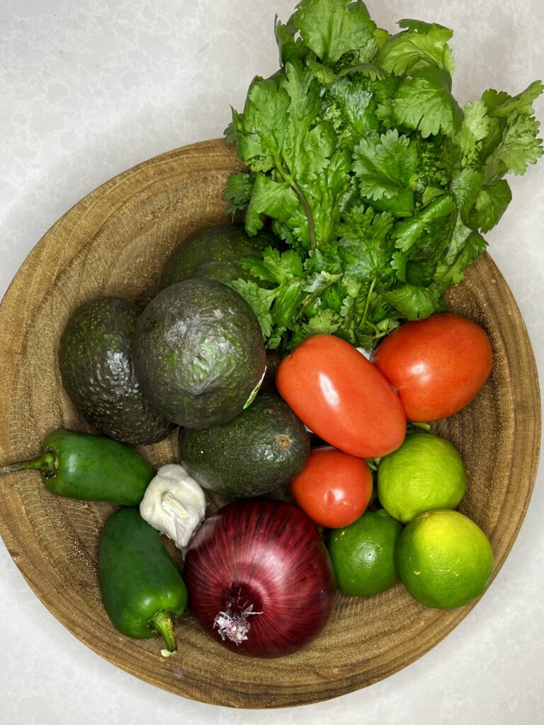 cilantro, avocados, tomatoes, limes, jalapeños, red onion, and garlic in a bowl