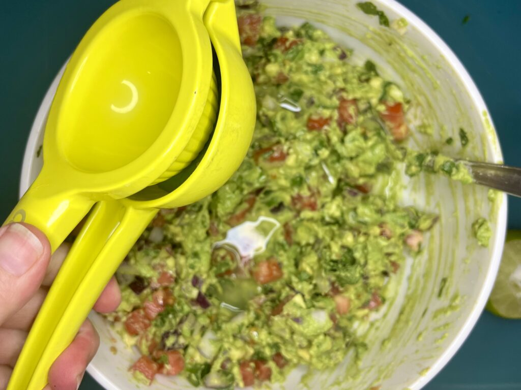 lime being squeezed into bowl with avocado and vegetables