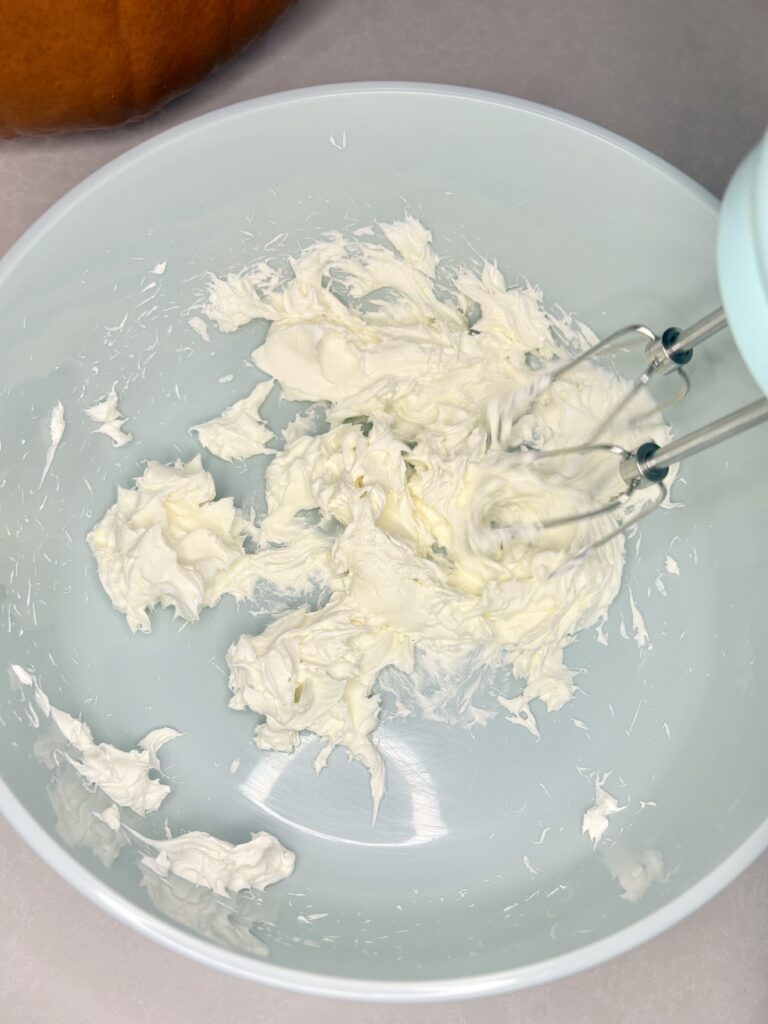 cream cheese in a bowl being mixed with a hand mixer