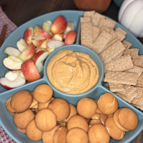 pumpkin dip in a serving tray with vanilla wafers, apple slices and graham crackers on a table