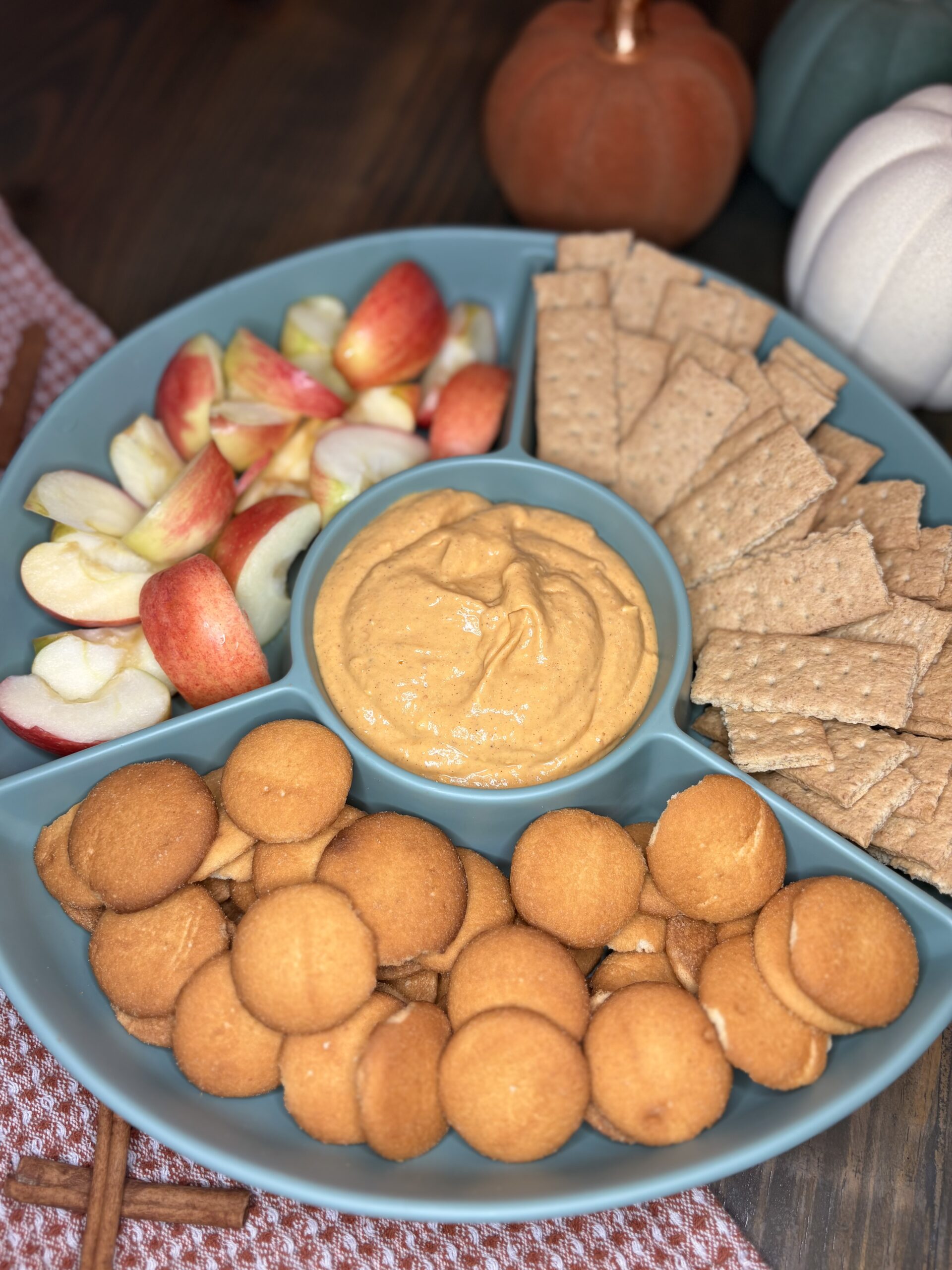 pumpkin dip in a serving tray with vanilla wafers, apple slices and graham crackers on a table