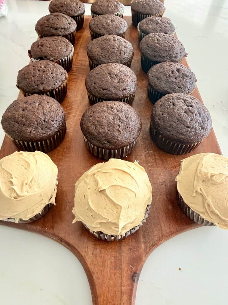 Three frosted cupcakes, and then the rest of the cupcakes would be about 15 of them unfrosted on a brown cutting board on the counter.