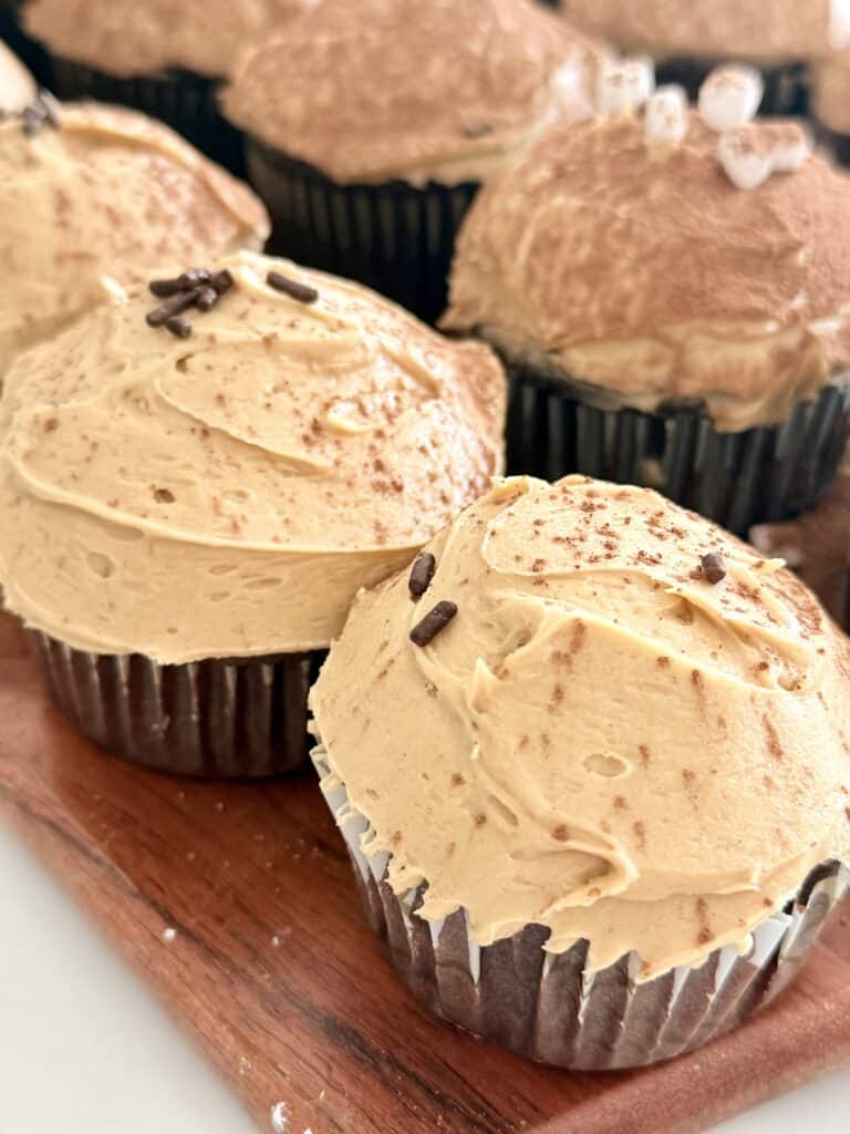 Frosty cupcake cupcakes with chocolate sprinkles on a brown cutting board.