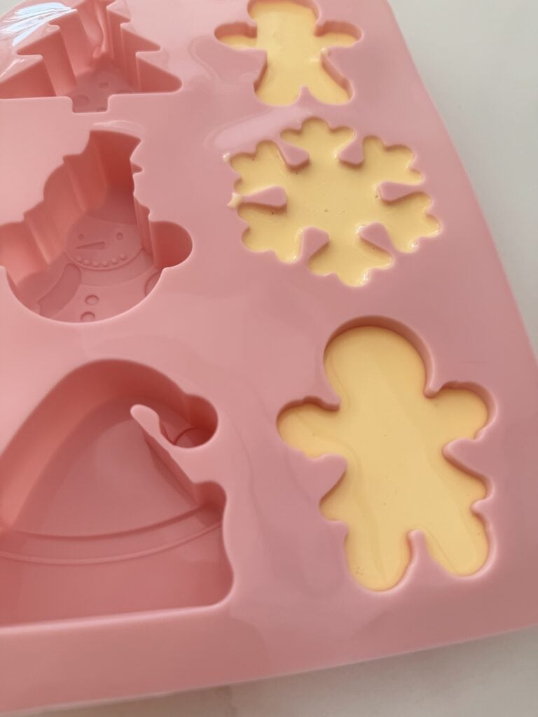 Festive Christmas ice molds in the shapes of gingerbread men and snowflakes. In a pink festive silicone tray. On the counter.