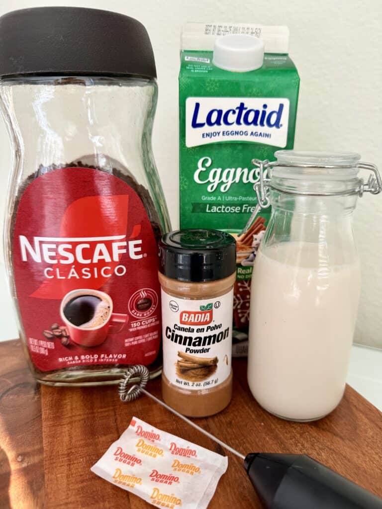 instant coffee, eggnog, cinnamon and milk with a sugar packet and frother on the brown board counter.
