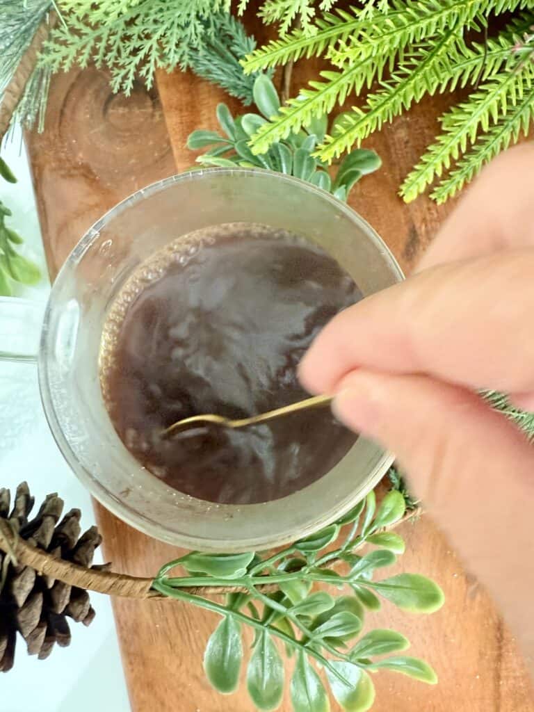 using a spoon to stir warm water with sugar and instant coffee. surrounded by festive greenery.