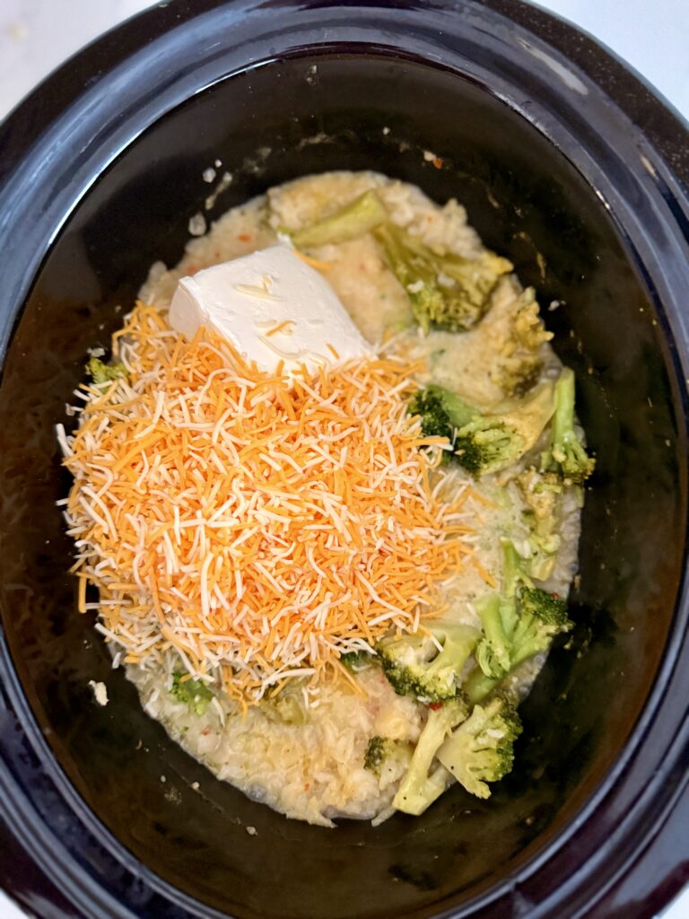 Shredded cheese, cream cheese, broccoli and rice and broth in the slow cooker on the counter.