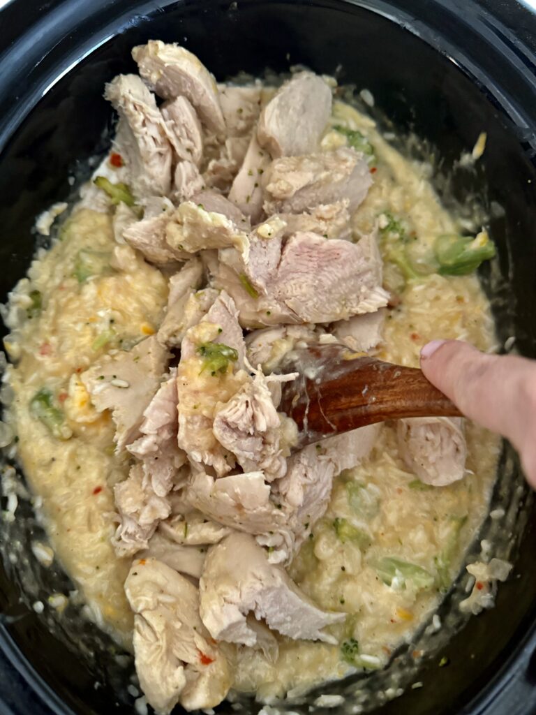 Sliced chicken on top of ingredients in a black slow cooker on the counter.