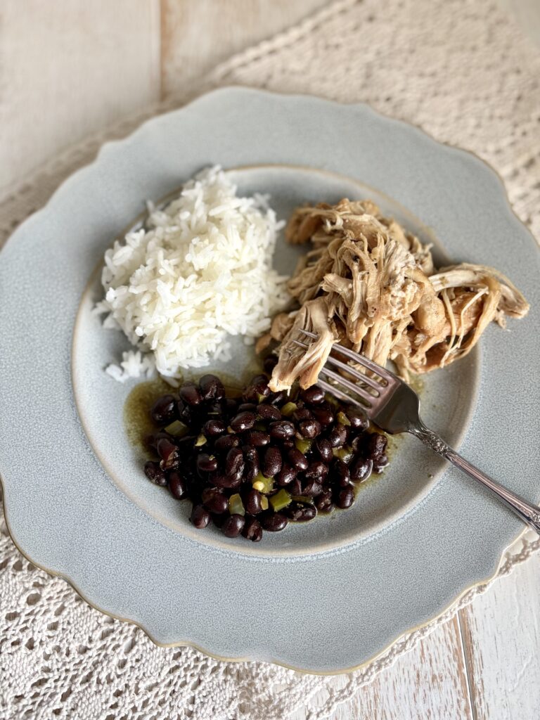 Juicy shredded chicken, white rice, black beans, and a fork on a pastel blue plate, served on a woven tablecloth. Perfect comfort food and easy dinner idea, nutritious and delicious meal for the family.