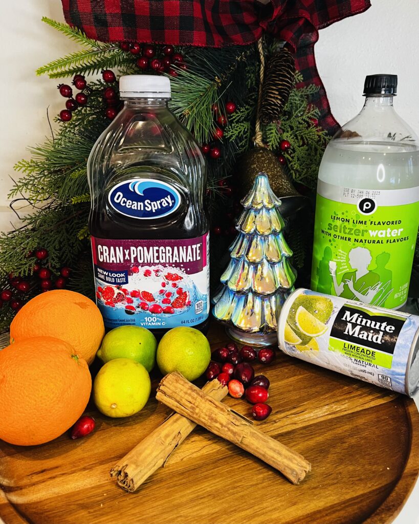 crab-pomegranate juice, oranges, limes, cinnamon sticks, whole cranberries, lim seltzer water, limeade frozen on a brown tray on the counter.