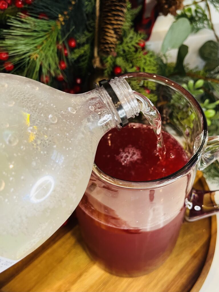 lime seltzer being poured into juice in a glass pitcher on a brown tray.