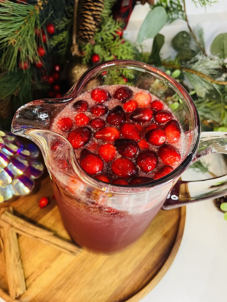 Cranberries in the Christmas punch in a large glass pitcher on a brown tray on the counter