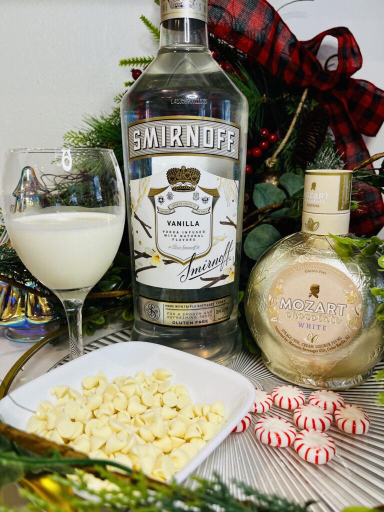 vanilla vodka, white chocolate liqueur, heavy whipping cream, white chocolate chip and peppermint candy on a glass tray on the counter.