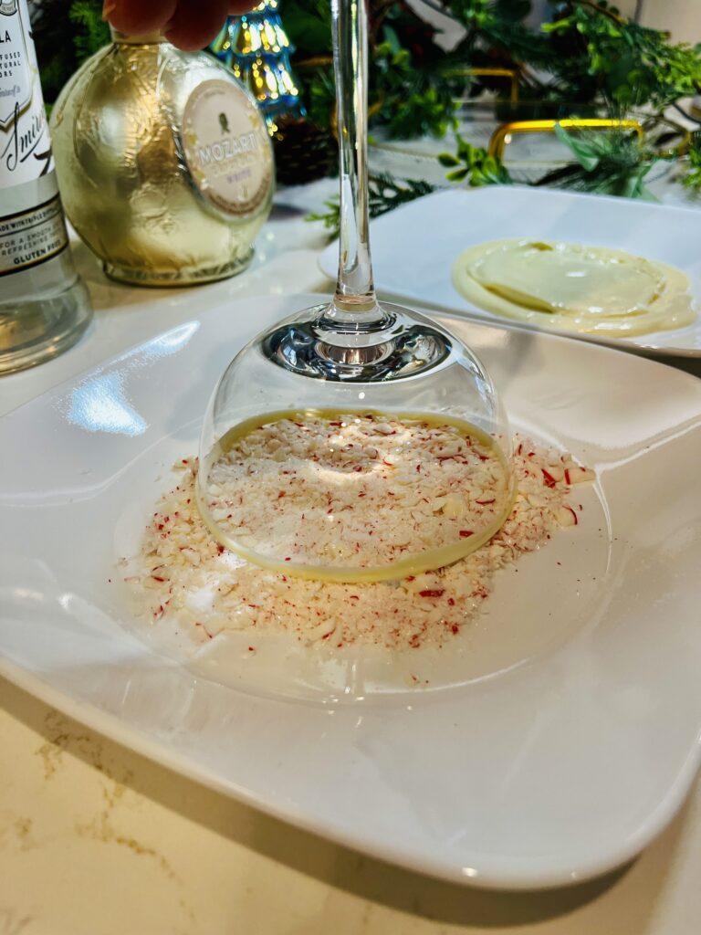 dipping a coupe glass int crushed candy on a white plate on the counter.