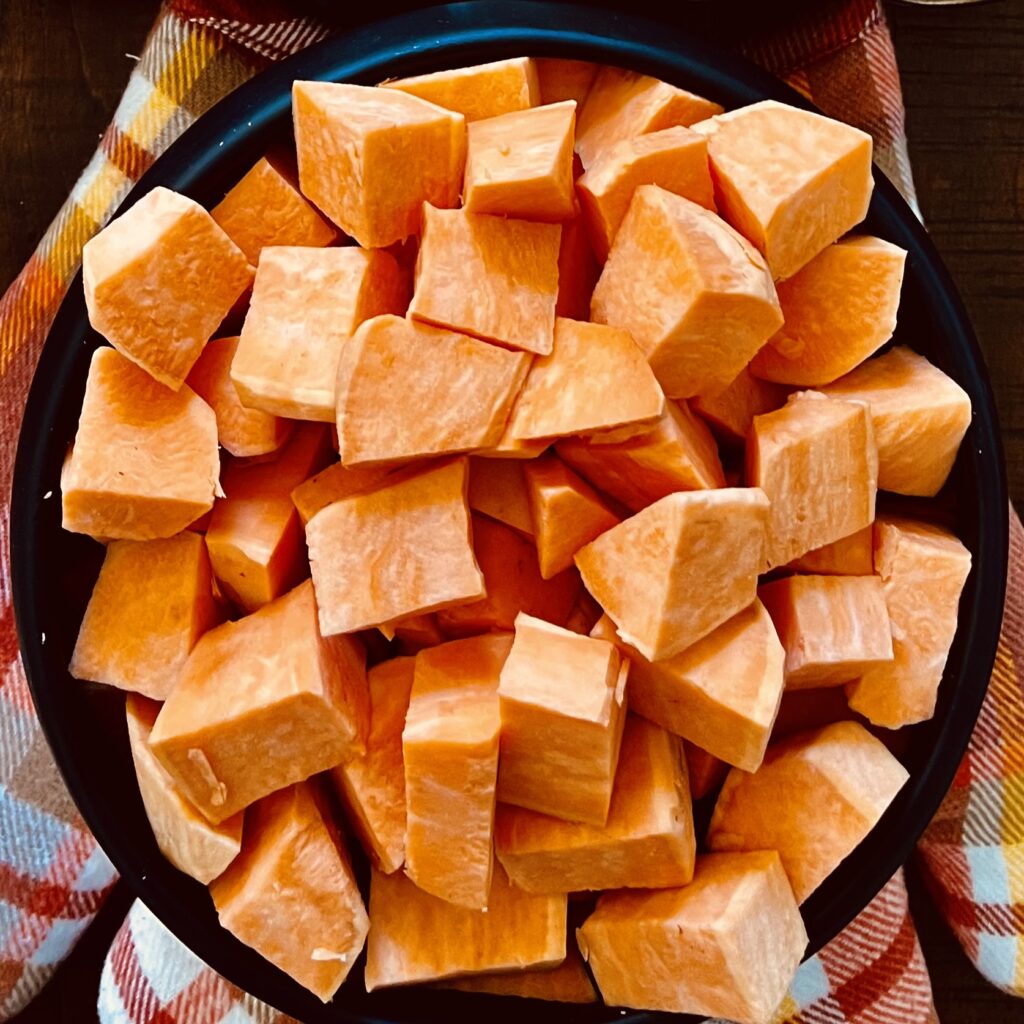 washed, peeled and cut sweet potatoes in a black bowl on orange oven hits on a table.