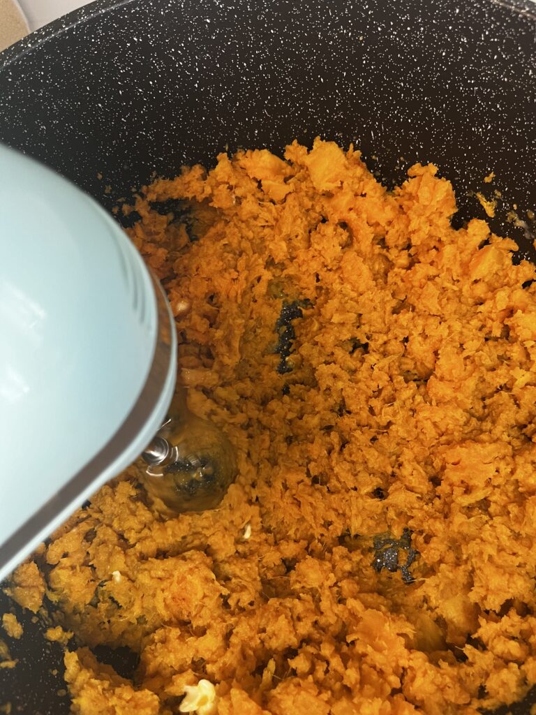 mashing sweet potatoes in a large black pot on the counter