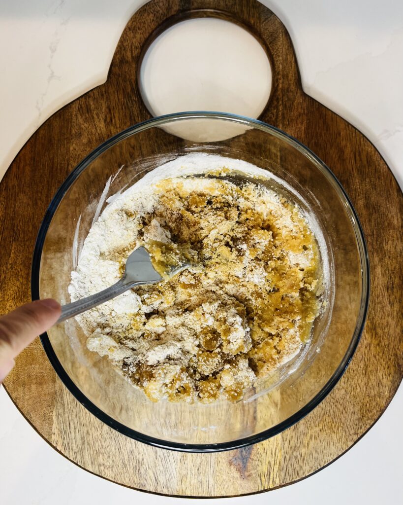 brown sugar topping being mixed with a fork in a small glass bowl on a brown cutting board on the counter