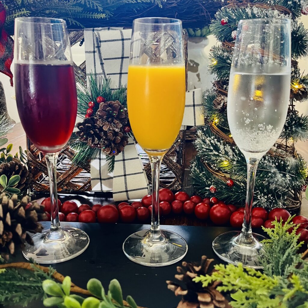 Champagne flutes with pom-cranberry juice, orange juice and lime seltzer water on a black table.