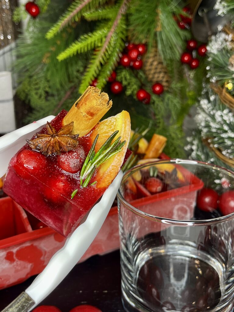 Placing a garland ice cube into a tumbler glass on a black cutting board on the counter