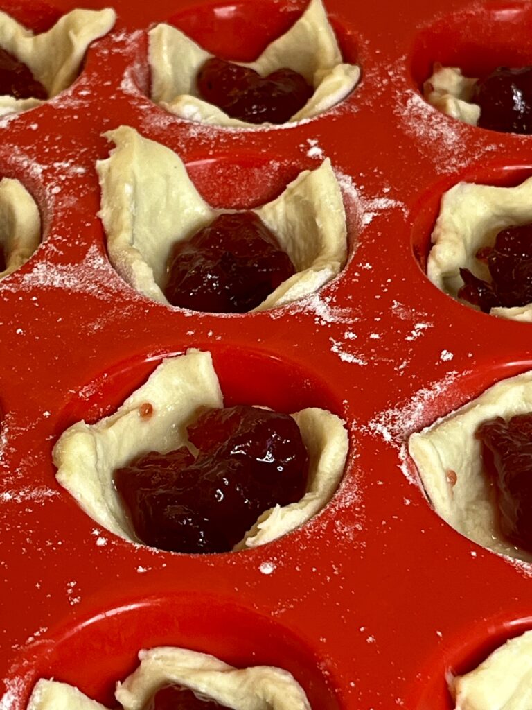 raw pastry with cranberry sauce in a red silicone mini muffin tray on the counter.