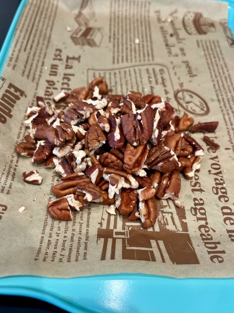 Broken up pieces of roasted pecans on a lined baking sheet on top of the stove.