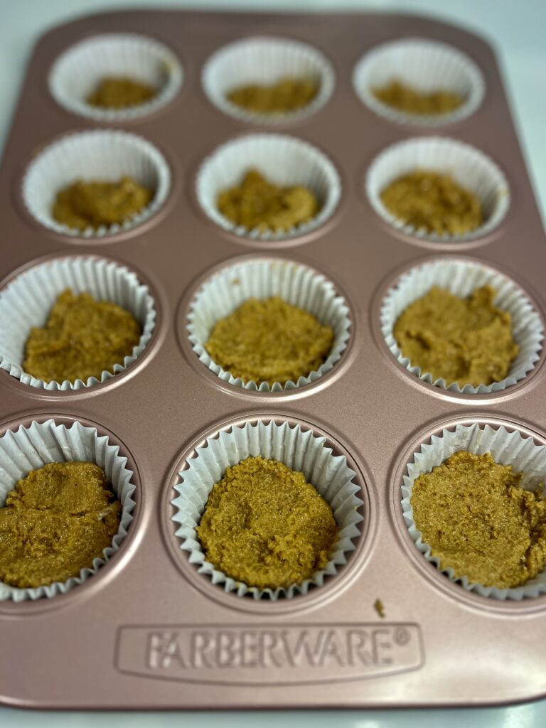 bottom gingerbread crust layer in paper muffin cups in a pink muffin tin on the counter.