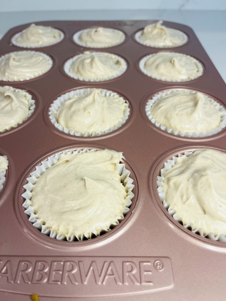 Gingerbread cheesecake filling in muffin tin paper cups in a pink muffin tin on the counter