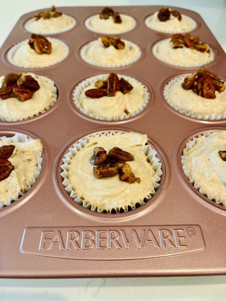 mini gingerbread cheesecakes topped with candied pecans in a pink muffin tin on the white counter