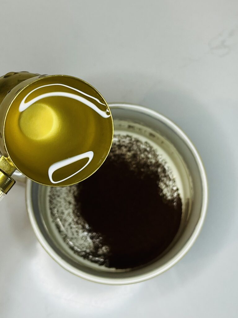 instant espresso a cup and water in a gold colored jigger with water in it, on the counter 