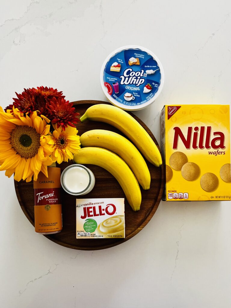 Nilla wafer cookies, Cool Whip, bananas, milk, instant vanilla pudding, caramel sauce and flowers on a brown tray on the counter