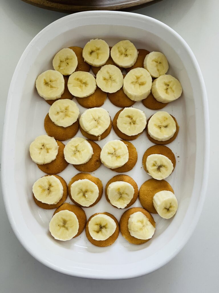 Sliced bananas on top of Nilla wafers in a white baking dish on the counter.