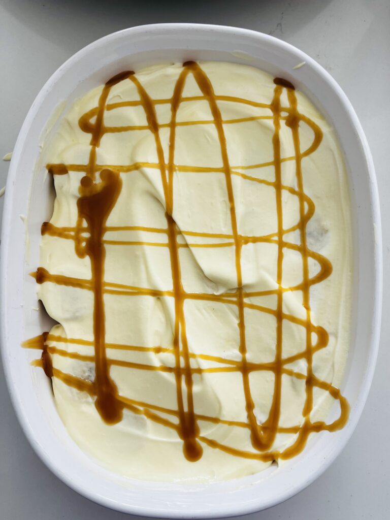 Vanilla pudding drizzled with caramel sauce in a white baking dish on the counter.