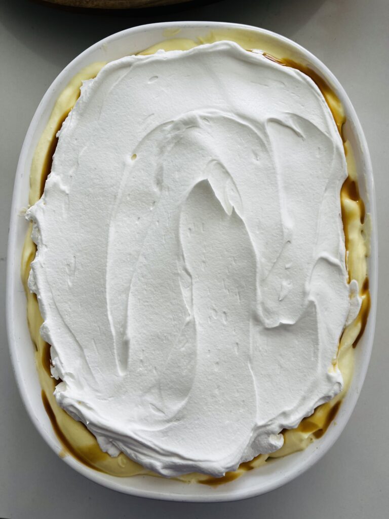 Cool Whip on top of vanilla pudding in a white baking dish on the counter.