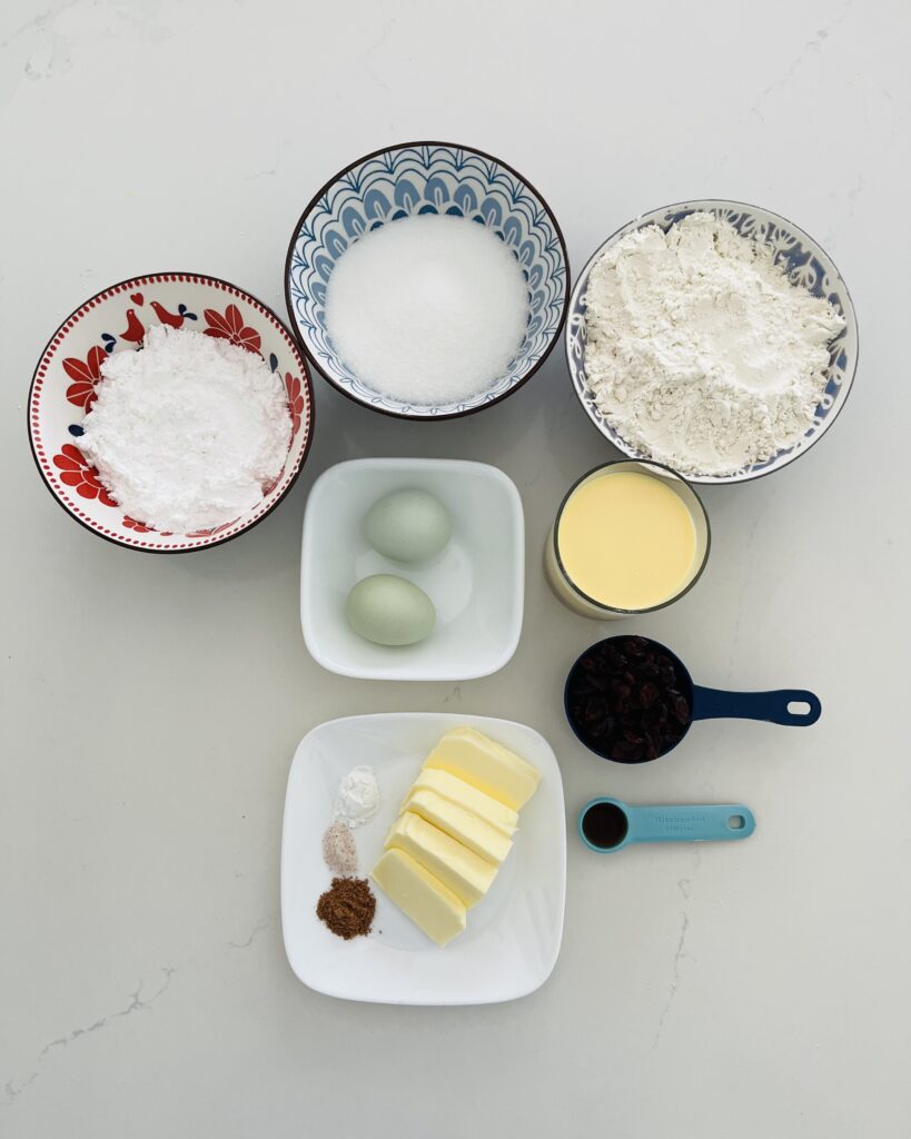 all purpose flour, sugar, dried cranberries, baking powder, salt, nutmeg, butter-softened, eggnog, eggs, vanilla extract and  powdered sugar in container on the white counter.