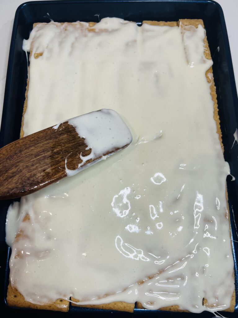 Spreading marshmallow mixture onto graham crackers in a blue baking sheet on the white counter.