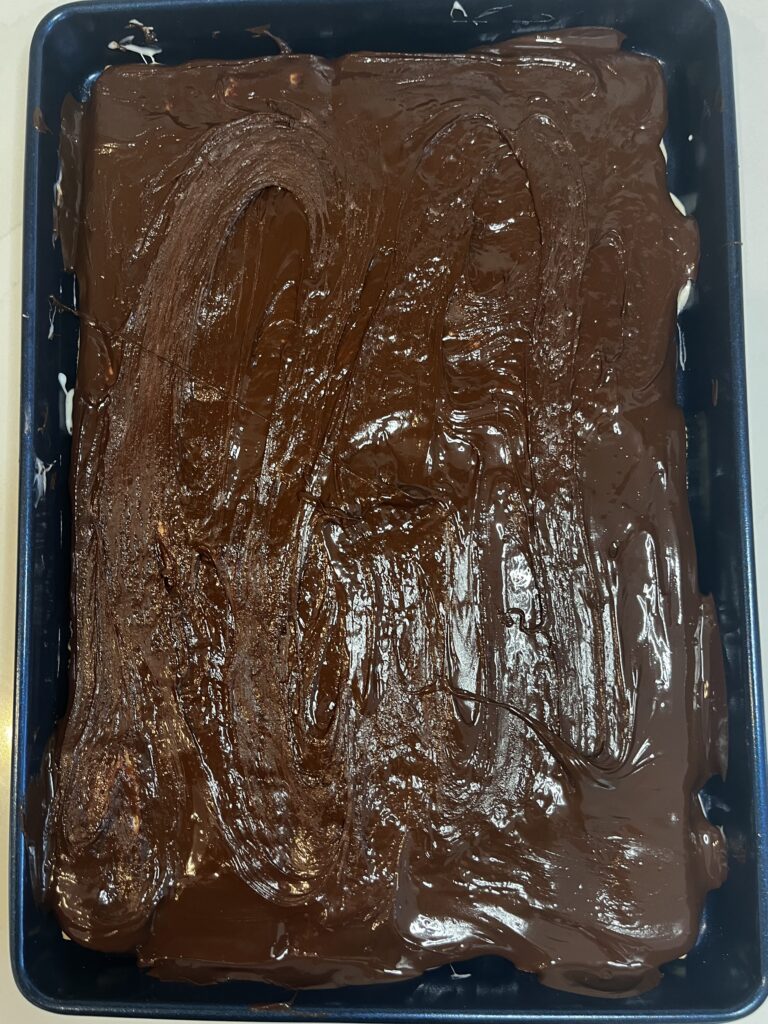 Melted chocolate poured over marshmallow layer in a baking sheet on the counter