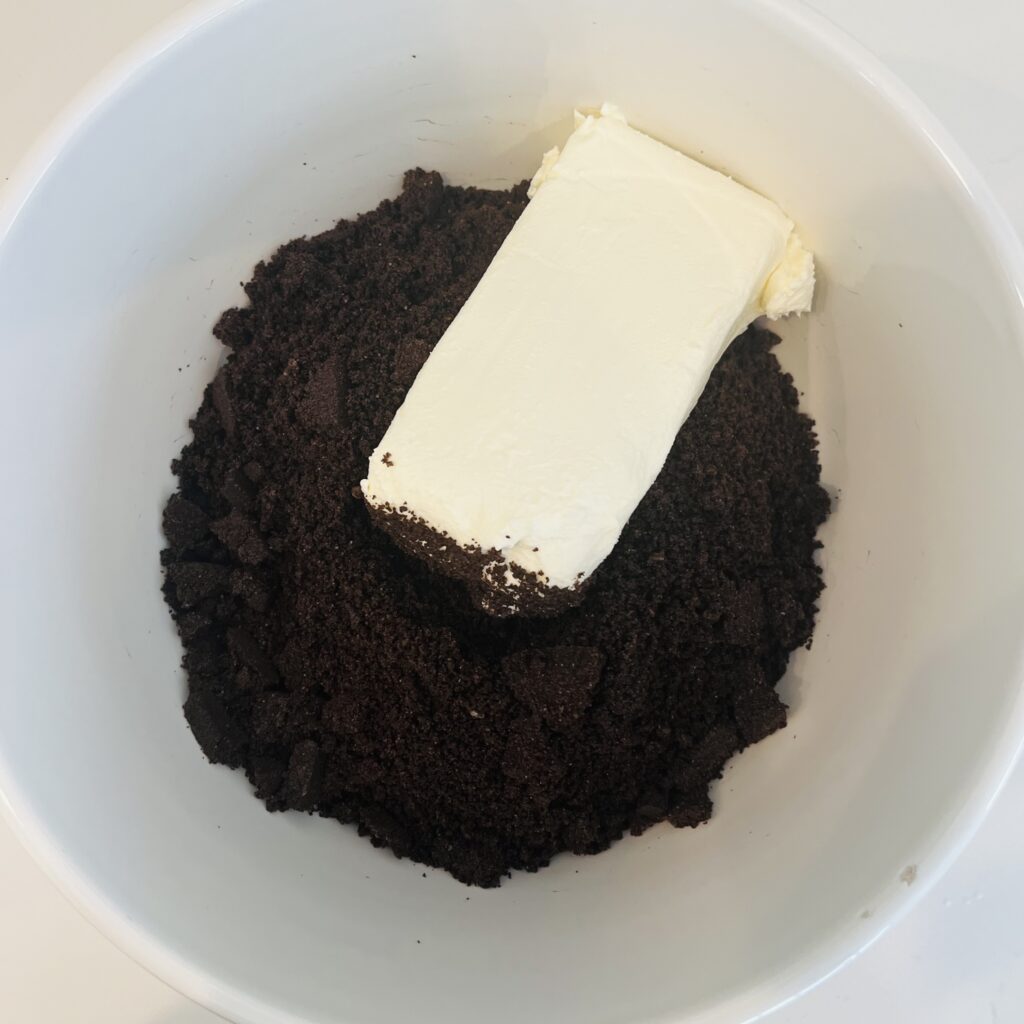 Cream cheese in a mixing bowl with the Oreo cookie crumbs on the counter