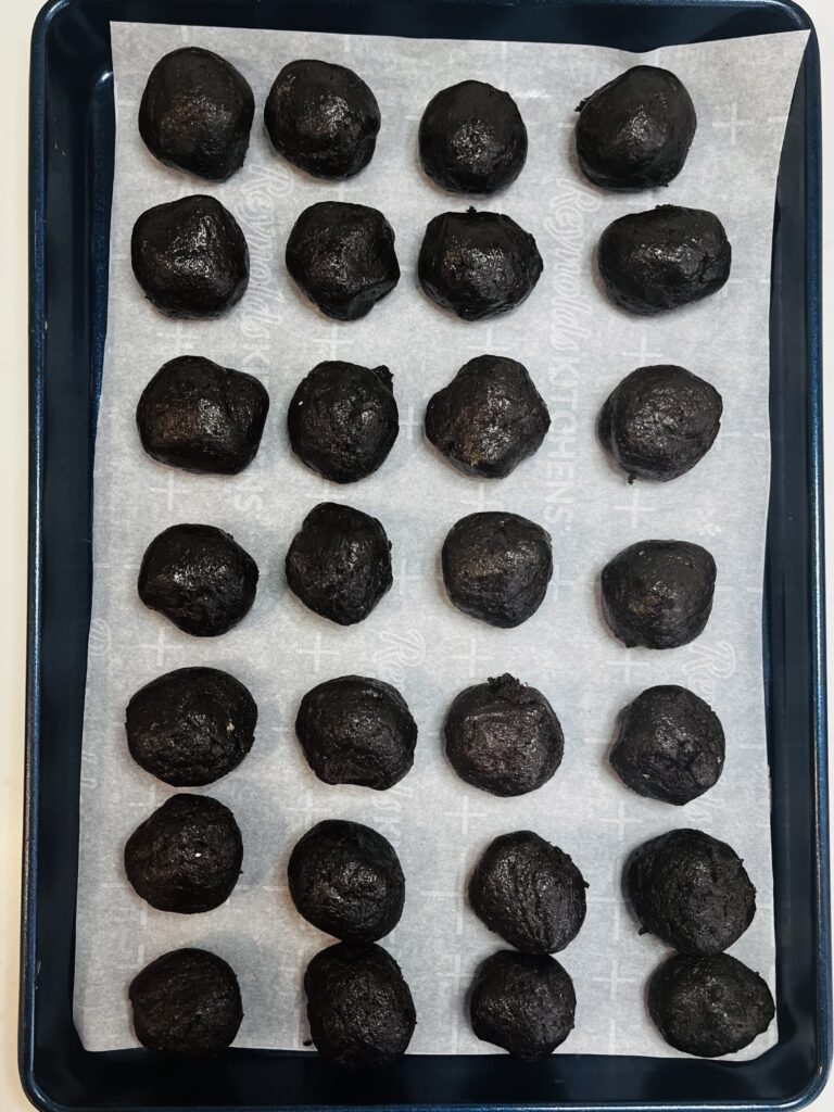 28 Oreo Balls on a parchment paper lined baking sheet on the counter