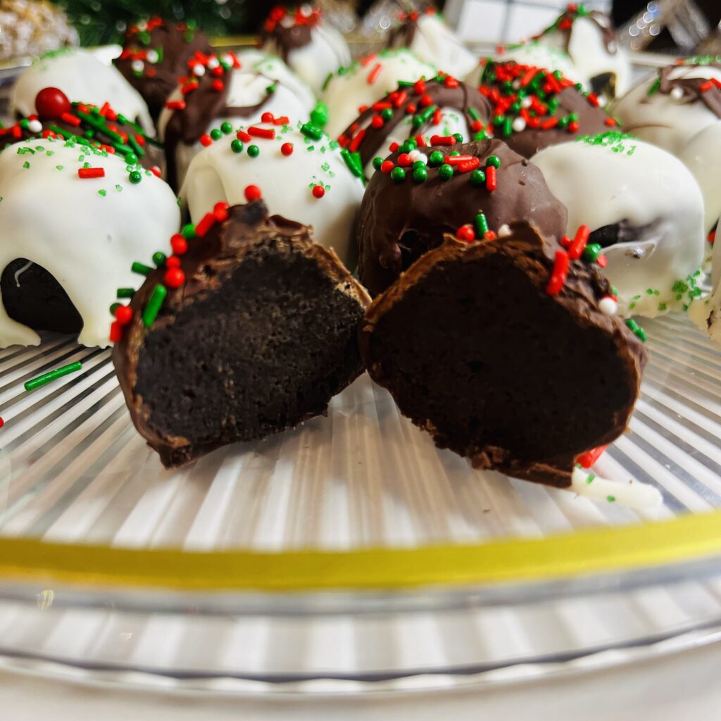 Festive Oreo Balls on a glass platter on the counter. One Oreo Ball cut in half exposing the Oreo cookie inside on the glass platter on the countertop 