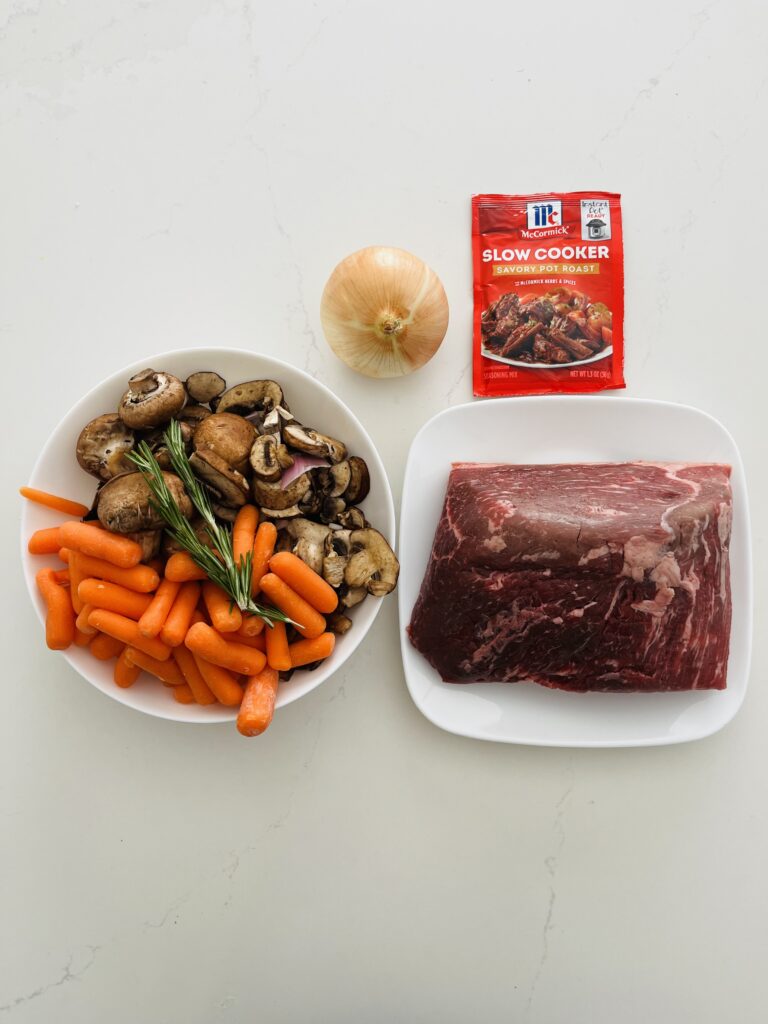 round roast on a white plate, *McCormick slow cooker seasoning mix, baby carrots, white mushrooms in a large white bowl, onion on the counter