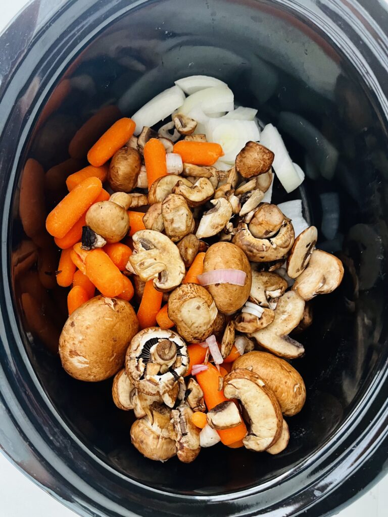 mushrooms, carrots, and chopped onion  in a black slow cooker on the counter. 