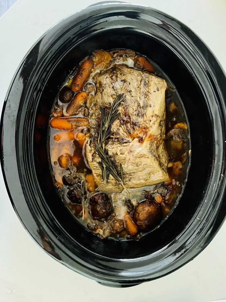 Hearty slow cooker pot roast and vegetables in a black slow cooker on the counter.