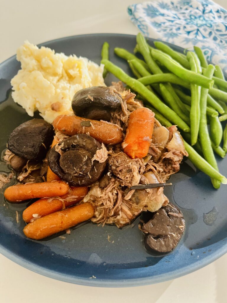 Slow cooker pot roast with mushrooms and carrots on a blue plate on the counter.