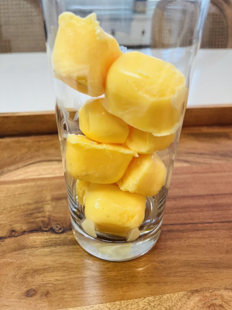 eggnog ice cubes in a tall glass on a brown tray on the counter.