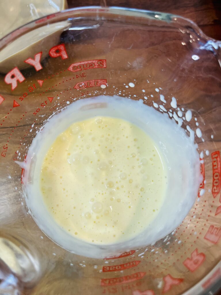 whipped and frothed eggnog in a glass measuring cup on a brown tray.