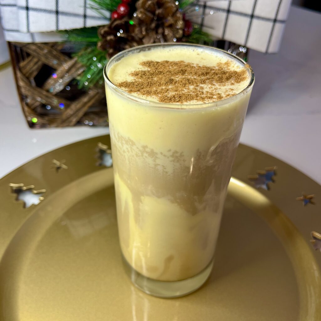 Iced eggnog coffee in a tall glass on a gold Christmas themed tray. Christmas decorations on the counter.