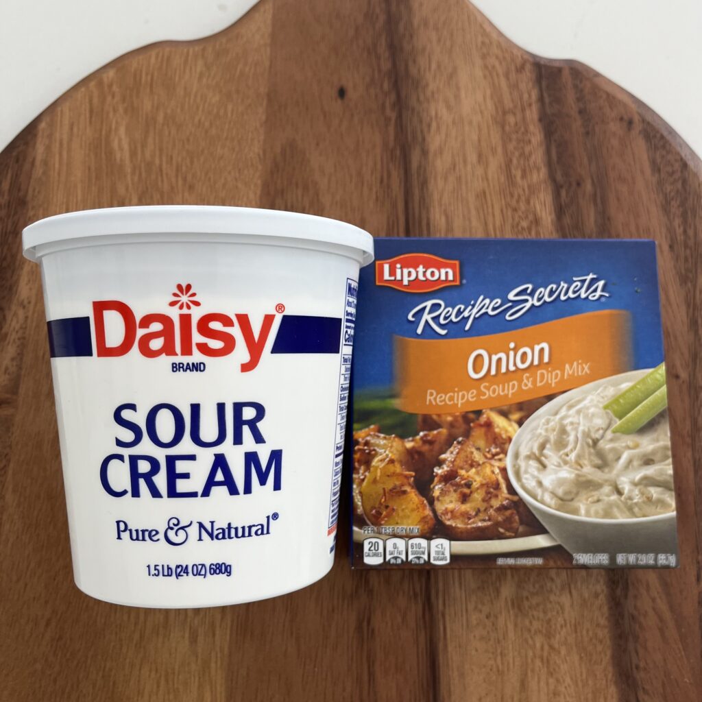 A container of sour cream and onion soup and dip mix on a brown cutting board on the counter.