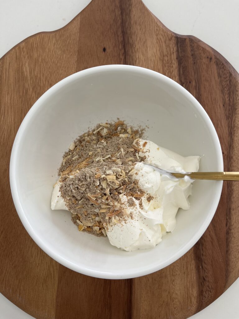 Dry onion soup mix and sour cream in a white bowl on a brown cutting board on the counter.